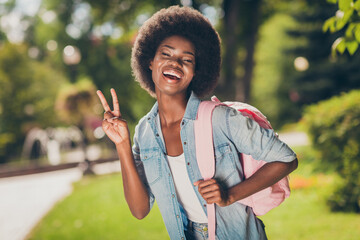 Poster - Photo portrait of black skinned girl smiling showing v-sign with two fingers laughing wearing denim shirt pink casual backpack