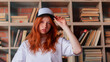 © oleg_ermak - Portrait of a redhead woman in template blank t-shirt and cap with healthy freckled skin. Young caucasian model posing on bookshelf background. Copy space and mock up. Place for adverising