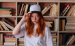 © oleg_ermak - Portrait of a redhead woman in template blank t-shirt and cap with healthy freckled skin. Young caucasian model posing on bookshelf background. Copy space and mock up. Place for adverising