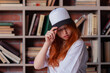 © oleg_ermak - Portrait of a redhead woman in template blank t-shirt and cap with healthy freckled skin. Young caucasian model posing on bookshelf background. Copy space and mock up. Place for adverising
