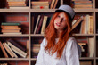 © oleg_ermak - Portrait of a redhead woman in template blank t-shirt and cap with healthy freckled skin. Young caucasian model posing on bookshelf background. Copy space and mock up. Place for adverising