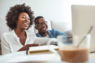 Happy couple with laptop spending time together at home. Happy young couple paying bills together and managing budget, sitting on the sofa and using calculator and laptop