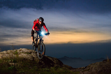 Cyclist Riding the Mountain Bike on Rocky Trail at Night. Extreme Sport and Enduro Biking Concept.