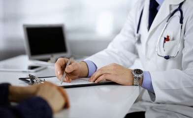 Unknown young woman patient discuss the results of her medical tests with a doctor, while sitting at the desk in a hospital office. Physician using clipboard for filling up medication history records