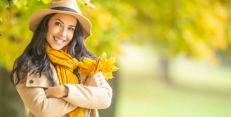 Beautiful girl holds arms crossed on her chest holding autumn leaves, smiling into the camera