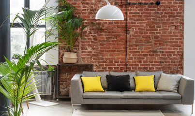 stylish sofa with yellow pillows and red brick wall in loft apartment in industrial style. interior 