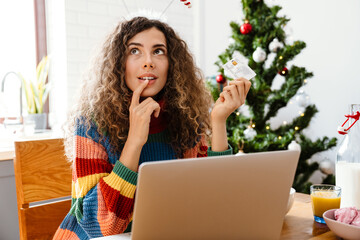 Thinking woman using credit card and laptop while having breakfast