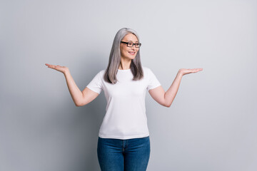 Poster - Photo of retired woman hold two palms look side empty space wear specs white t-shirt denim jeans isolated grey color background