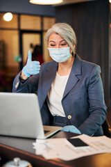 Sticker - Businesswoman in medical mask using laptop and giving thumbs up