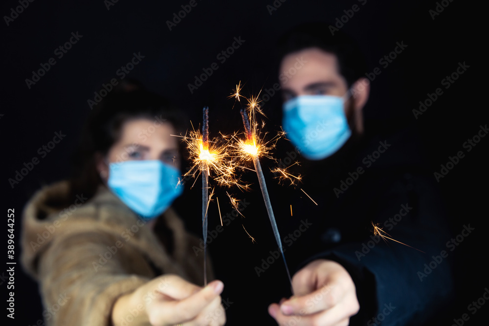 Young couple wearing protective face masks for Coronavirus and holding sparklers for New year's eve, 2021 and Covid-19 concept - obrazy, fototapety, plakaty 