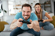 © JustLife - Husband and wife playing video game with joysticks in living room. Loving couple are playing video games at home..