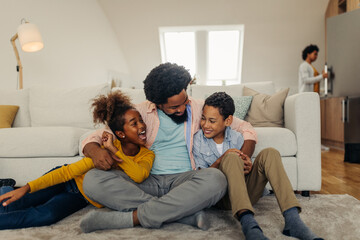 Wall Mural - Afro father and his children socializing having while sitting on sofa in the living room