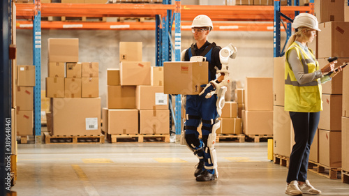 High-Tech Futuristic Warehouse: Worker Wearing Advanced Full Body Powered exoskeleton, Walks with Heavy Cardboard Box. Exosuit amplifies Human Performance, strength, Eliminates Work-Related Injuries