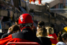 The Back Of The Search And Rescue Worker Blurred In Front Of The Building Destroyed In The Earthquake,watching And Resting