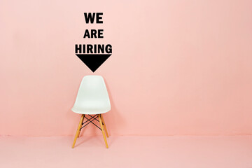 Job recruiting advertisement represented by 'WE ARE HIRING' texts on the wall. One chair to represent the hiring position to be recruited and filled.