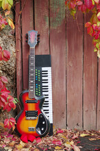 Electric Guitar, Guitar Case And Synthesizer On The Background Of A Fence And Autumn Leaves.