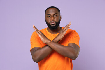 Wall Mural - Serious young african american man 20s wearing basic casual empty blank orange t-shirt standing showing stop gesture with crossed hands isolated on pastel violet colour background studio portrait.