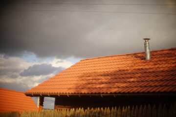 Red tile roof with galvanized chimney chimney against cloudy sky