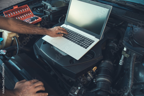 Professional car mechanic working in auto repair service using laptop