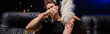 © LIGHTFIELD STUDIOS - Macho man drinking champagne, holding hand on woman leg sitting behind on sofa, while confetti falling in nightclub, banner