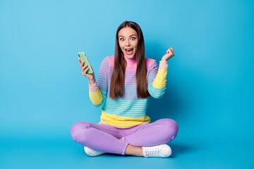 Poster - Portrait of glad cheerful girl sitting lotus position crossed legs using gadget browsing media isolated on bright blue color background