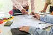 © amnaj - Group of architects planning together at desk with blueprints.