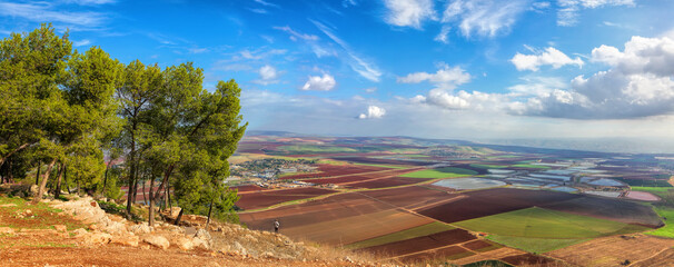 Panoramic agricultural landscape. Nature view on Jezreel beautiful valley from Mounts Gilboa. Men stands on the top and looks at plowed land, colorful fields, fish ponds. Northern District of Israel