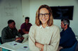 © Prins Productions - Caucasian business woman standing confidently with cross-arms in front of male colleagues in board room during team meeting