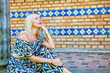 © wernerimages - blond woman in colorful dress sitting outdoors by a pillar