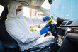 © Konstantin Zibert - Disinfection professional cleans up a steering wheel of a car with a yellow rug. Sanitary service worker disinfects the vehicle's driver seat place. Covid-19 spread prevention. Health concept.