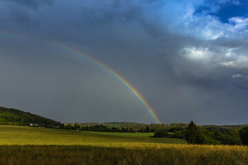  Double rainbow in countryside. Beautiful intense rainbow colors in rainy day.Weather forecast.Fall rural landscape with rainbow over dark dramatic stormy sky.Freedom happiness concept