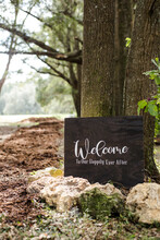 Painted Wooden Wedding Welcome To Our Happily Ever After Sign In Foreground With Walking Path And Forest In Background