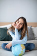 © BestForYou - Happy young woman  sitting on the bed at home with a globe dream to trip. Enjoy freedom alone.
