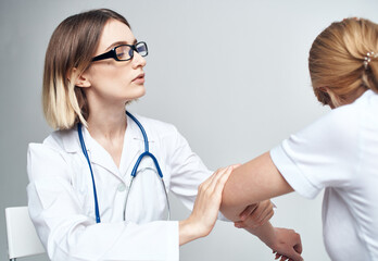 doctor examines the patient bending his arm on a light background and a stethoscope