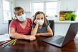 © SB Arts Media - Coronavirus school closures and lockdown. Mum and bored daughter with masks studying online at home