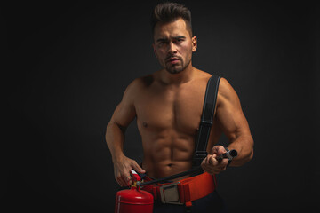 Wall Mural - portrait of a muscular, handsome firefighter on a dark background, holding a fire helmet, looking to the side