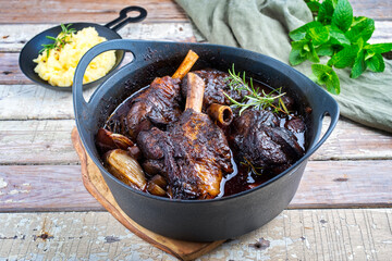 Wall Mural - Modern style traditional braised slow cooked lamb shank in red wine sauce with shallots and mashed potatoes offered as close-up in a design stewpot