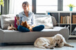 © nenetus - Attractive young woman using mobile phone while sitting in couch with her dogs and cat in living room at home.