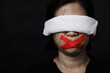 © sorapop - Slave Asian woman blindfold wrapping mouth with red adhesive tape, tied with chains and closed her eyes black background. Freedom speech censorship and stop talk, International Human Rights day