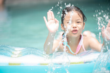 Wall Mural - .happy little girl playing with inflatable ring in outdoor swimming pool on hot summer day. kids learn to swim. child water toys. children play in tropical resort. family beach vacation.