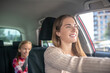 © zinkevych - Smiling mom driving with her daughter sitting on backseat of car