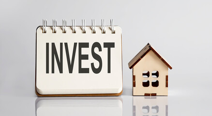 invest words written in an office notebook with wooden house. Financial Business concept.