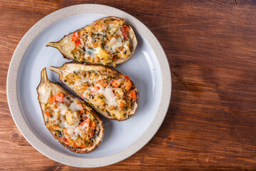 Halved eggplant baked with vegetables and cheese on a plate on a wooden table, close-up, top view, copy space