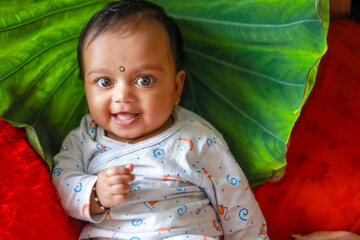 Canvas Print - Cute indian little child playing on bed with green leaf background