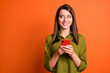 © deagreez - Photo of positive girl hold telephone look side empty space wear green shirt isolated orange color background