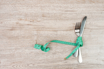 Wall Mural - Top view Green Measuring tape wrapped around fork and knife on wooden table background. dieting, weight loss, obesity and food control concept