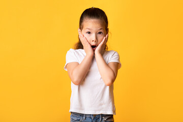 Wall Mural - Asian girl with open mouth touching cheeks in excitement