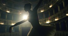 Cinematic Shot Of An Young Graceful Classical Ballet Female Dancer In White Tutu Is Performing A Choreography On Classic Theatre Stage With Dramatic Lighting Before Start Of A Show.