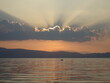 promienie zachodzącego słońca oświetlające chmury nad jeziorem, po którym płynie łódź