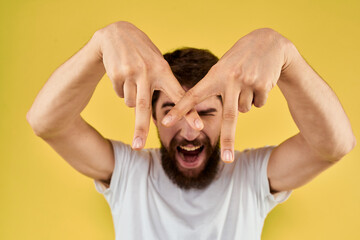 Bearded man emotions fun gesture with hands white t-shirt close-up yellow background